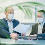 Deux hommes portant un masque de protection et signant des papiers